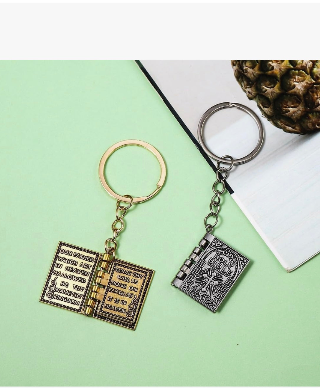 Two keychains shaped like open books with decorative covers on a green surface.